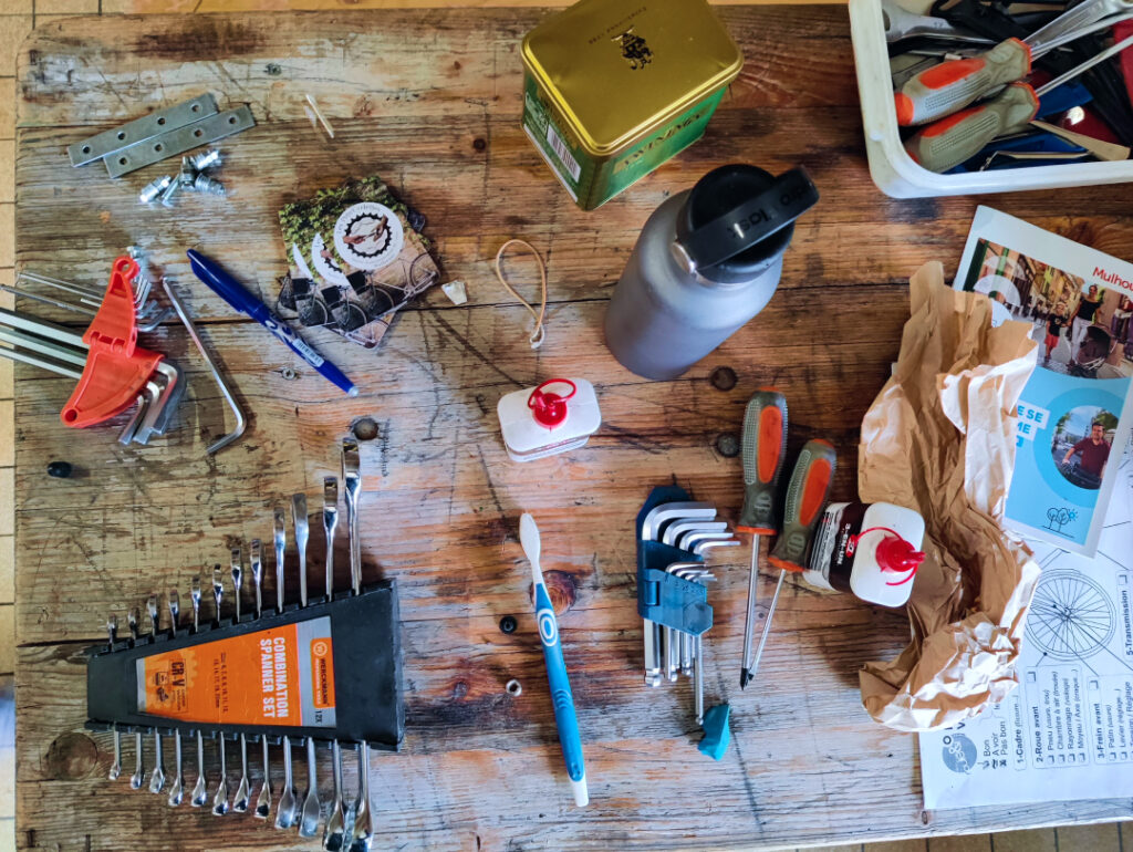 Vue du dessus d'une table d'atelier avec plusieurs outils disposés dessus : graisse, stylo, clés plates et tournevis