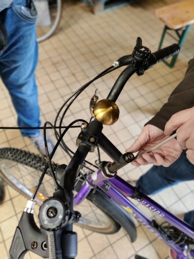 Un adhérent resserre la potence de son vélo sous les conseils d'un bénévole